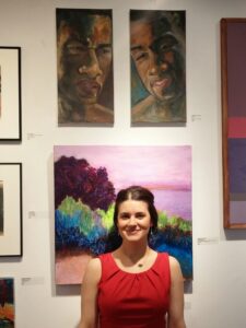 Stephanie stands next to her painting with two panels featuring a black male figure with a happy and sad face.