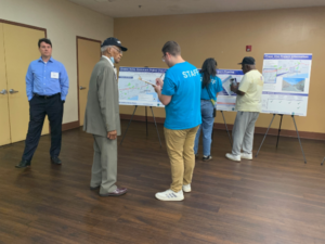 David standing to the right of a community member holding a clipboard and writing down their comments at a public open house