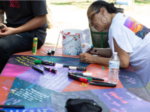 A community member writes on a collaborative community mural for the Framing the Future of the Roundhouse project.