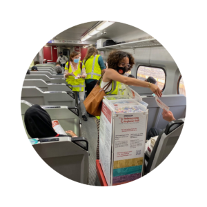 Staff in high vis gear pass out snacks and surveys on a regional rail car