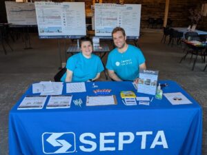 A woman and a man sitting down at a welcome table with materials for an Open House event