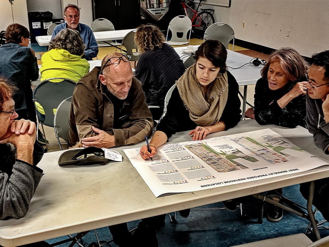 Meg sitting at a table with four public members and writing on a large diagram of public restroom locations as residents share their perspectives.
